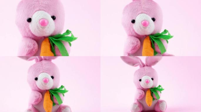 带有橙色小胡萝卜的粉红色复活节毛绒兔子玩具坐在柔和的背景上，特写镜头，慢动作。春季宗教节日的概念。