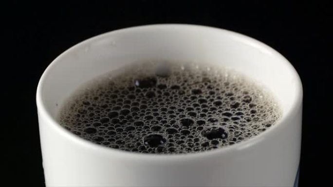 白色气泡在带有咖啡慢动作的杯子中完美地破裂。