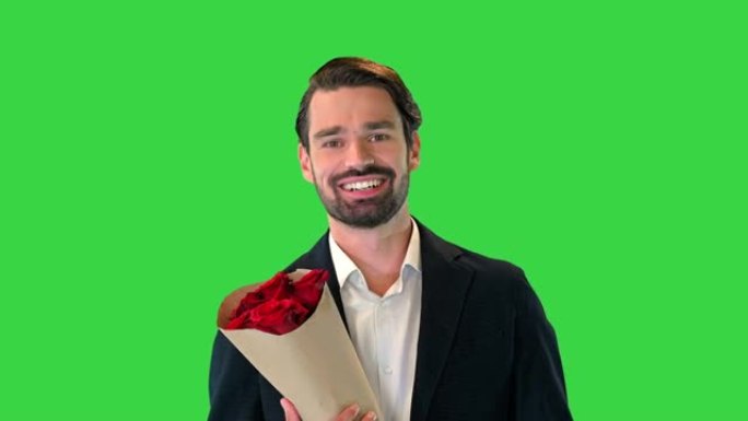微笑的英俊商人拿着玫瑰，看着相机在绿屏上调情，色度键