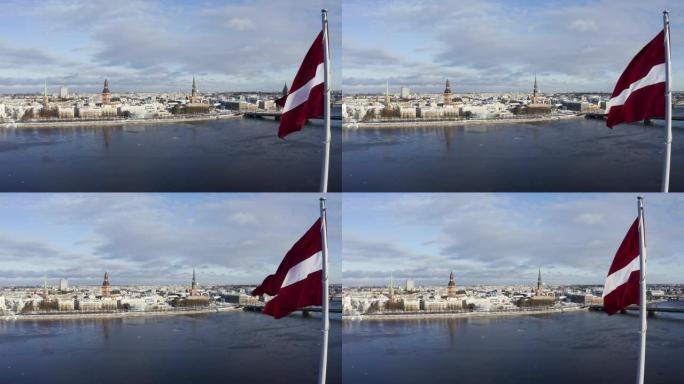 在美丽阳光明媚的冬日里，里加的城市全景，前景中有一面巨大的拉脱维亚国旗。背景是魔法古城里加。拉脱维亚