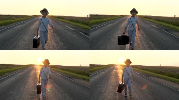 带手提箱的可爱快乐小男孩，夏天日落时走在乡村路上的复古相机