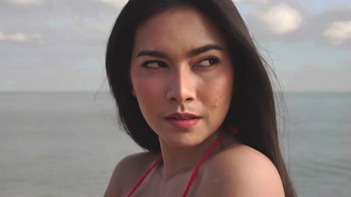 穿着比基尼的年轻亚洲美女在镜头前看起来性感的肖像。夏天天气下，热带海滩上的头发随风吹来。旅行和生活方