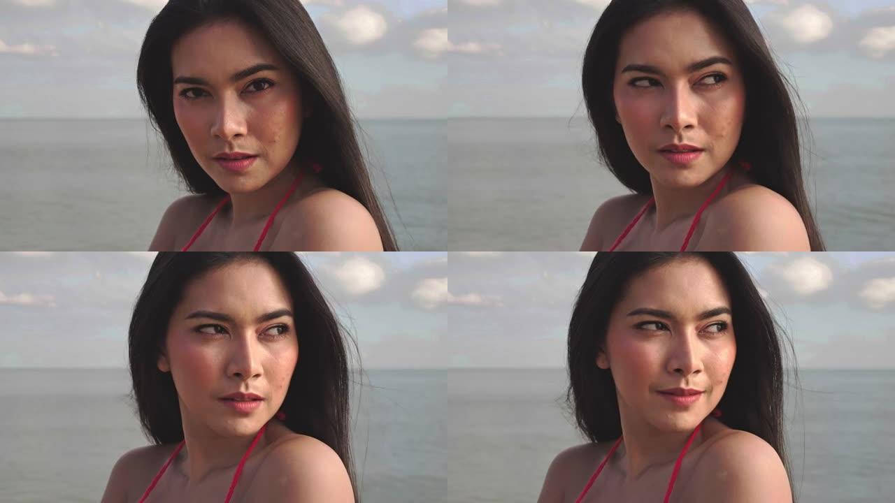 穿着比基尼的年轻亚洲美女在镜头前看起来性感的肖像。夏天天气下，热带海滩上的头发随风吹来。旅行和生活方