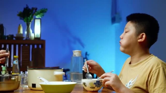 快乐的亚洲男孩吃寿喜烧或sha锅，火锅将食物与家人与led灯混合在一起，生活方式理念。