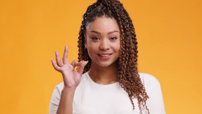 年轻酷的非洲裔美国妇女表现出不错的手势，对相机微笑，橙色工作室背景