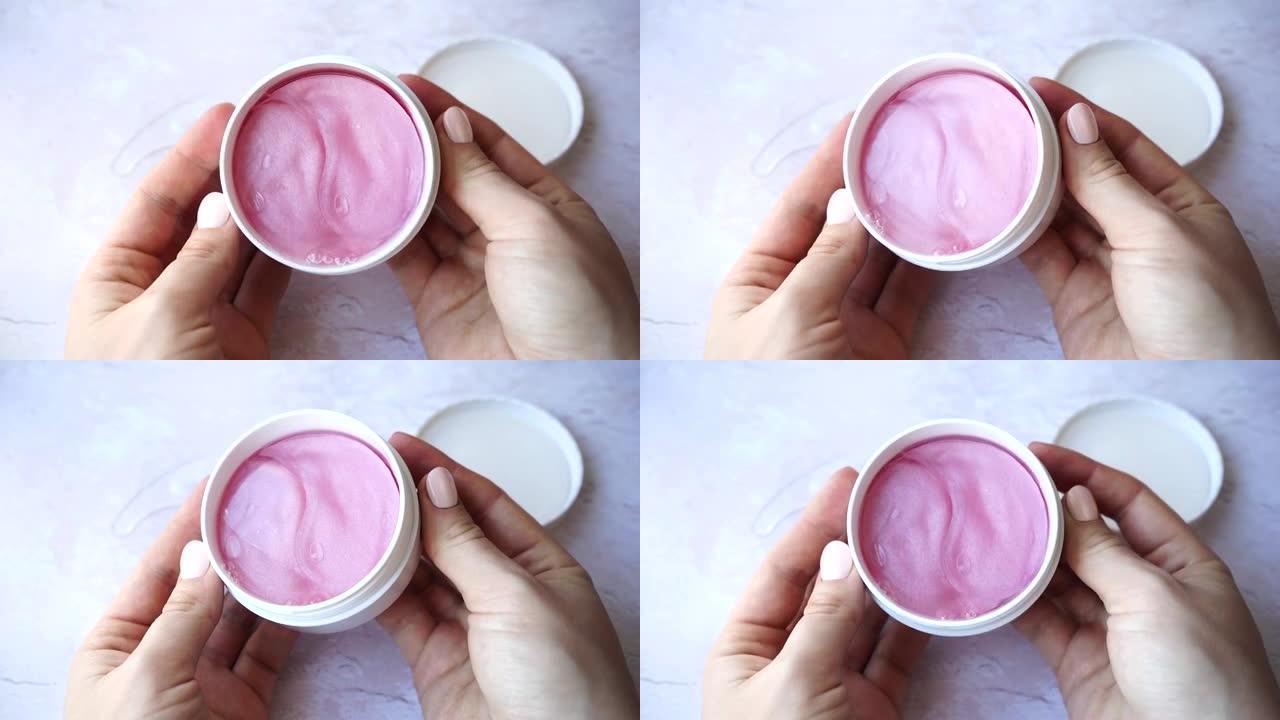 女性手中的水凝胶粉色化妆品眼贴罐。