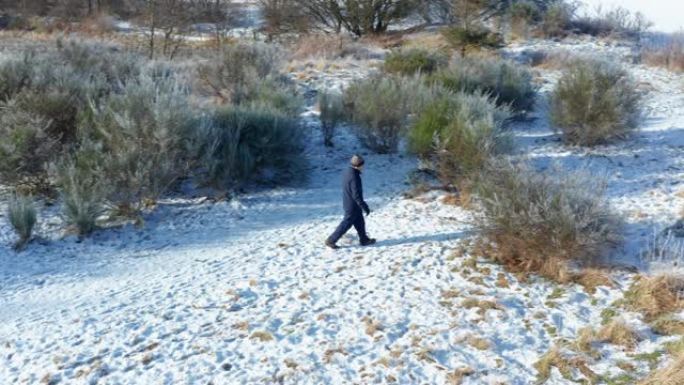 苏格兰西南部积雪覆盖的人行道上，一名高级男子独自行走的无人机的后视图