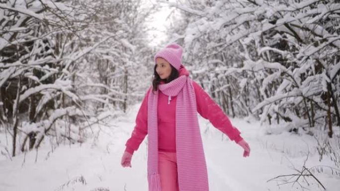 穿着粉红色衣服的女人戴着扎好的帽子和围巾穿过雪地