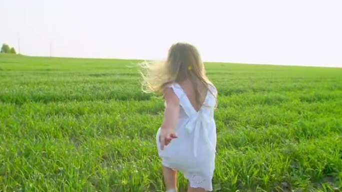 穿着白色连衣裙的金发小可爱女孩在绿色的田野上奔跑，微笑着。孩子，孩子在花园里跑，笑。美丽，自然，爱，