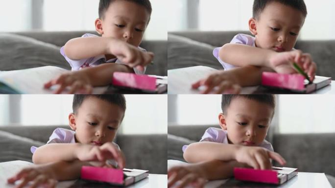 亚洲男孩用心做作业。男孩拿着铅笔写字，男孩在桌子上的白纸上画画，小学和家庭教育，远程在线教育概念。