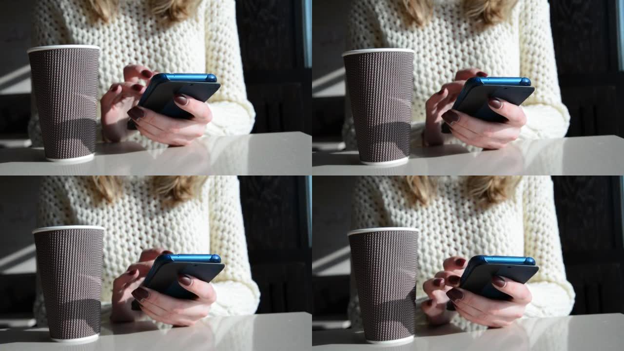 一个女人的手在智能手机上发短信时抓着咖啡杯，不倒翁