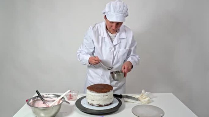 一位中年妇女面包师将糖浆倒入带有巧克力布朗尼的婚礼蛋糕上。