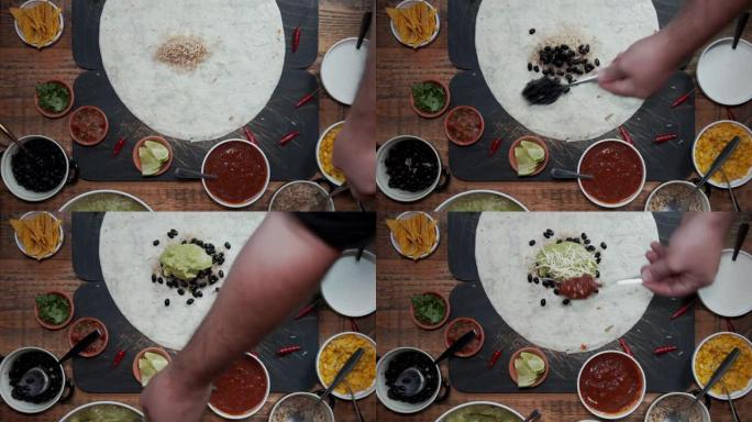 通过添加各种新鲜健康成分来准备玉米饼的手的俯视图。用新鲜蔬菜、萨尔萨酱米饭和豆类制作墨西哥风味墨西哥