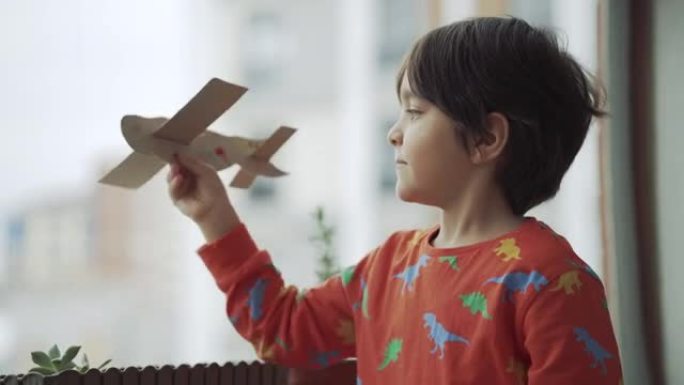 男孩在家里阳台玩纸飞机。纸飞机。儿童飞行手工飞机。小学生做了一架纸飞机，玩它。