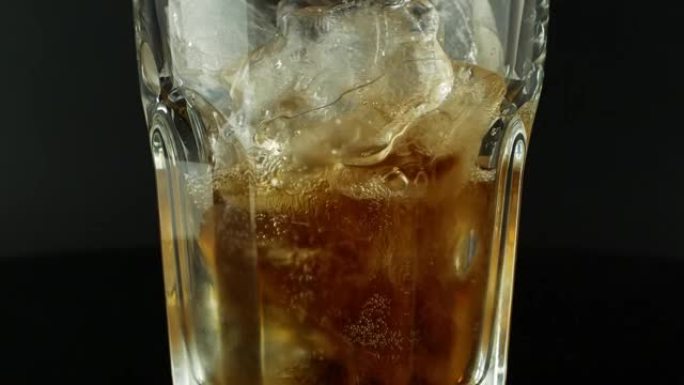 用冰块倒可乐特写。黑色背景上的玻璃里有冰和气泡的可乐。视频特写4k视频清爽的夏季饮料。食物和饮料。