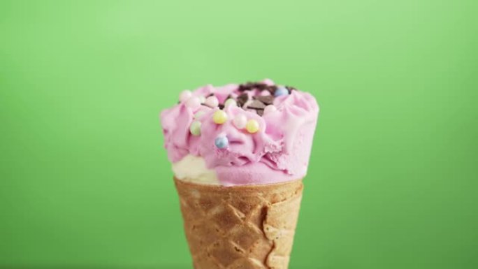浆果冰淇淋蛋卷，绿底有巧克力片，旋转。五颜六色的糖洒在美味的自制白色和粉红色冰淇淋上。
