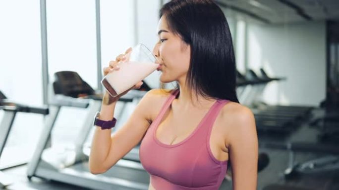 运动结束后，这位年轻漂亮的亚洲女子在体育俱乐部的酒吧里喝奶昔。这位女士穿着运动胸罩，身材苗条。这种饮