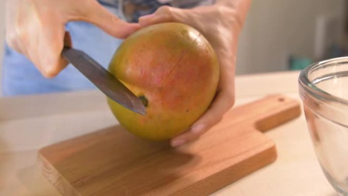 年轻女子用陶瓷刀在木砧板上切碎芒果。绿色冰沙排毒配方一步一步