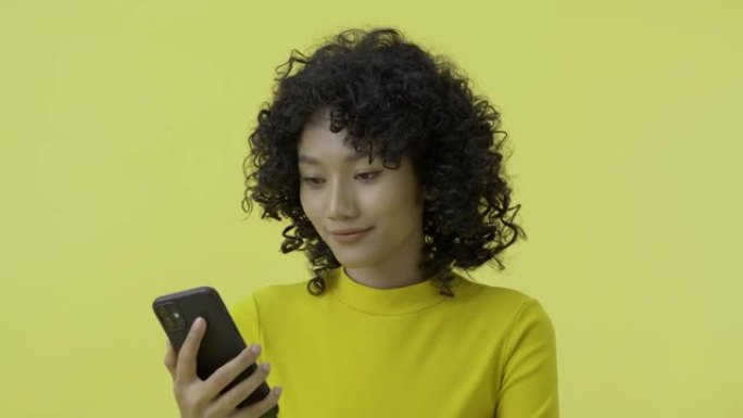 黄色背景下使用智能手机的美女肖像。她用自己的声音来指挥电话。
