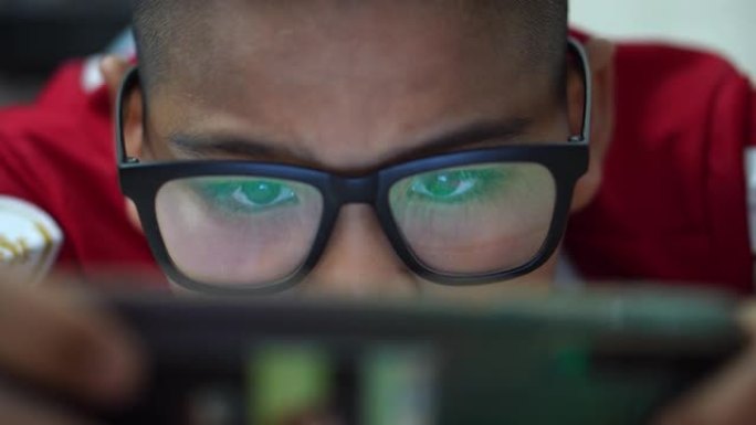一个戴眼镜的男孩用智能手机玩游戏娱乐。