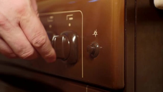 现代燃气灶上的手动扭转旋钮。男人在烤箱按钮上打开温度。特写