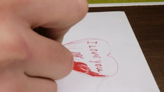 一个年轻人的手的特写镜头他用红笔在纸上写下我爱你的话