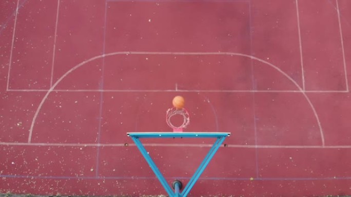 篮球篮板上方的高顶角橙色球干净击中篮筐并在室外场地慢动作得分