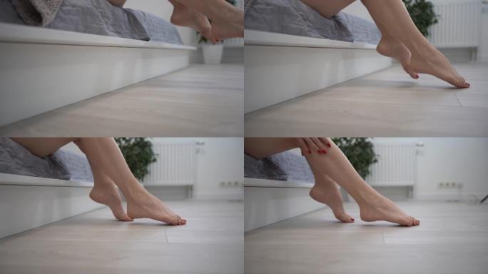 特写拍摄。女性下床的腿。背景浅，早晨醒来。白色床女性脚趾。去地板上。镶木地板或层压板。健身腿