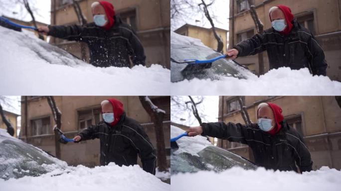 活跃的高级男子，由于新型冠状病毒肺炎爆发，戴着防护面罩，用塑料刮冰刀和扫帚清除汽车挡风玻璃上的雪