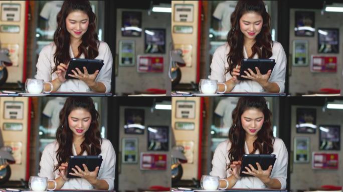 美丽迷人的亚洲女商人使用电脑平板电脑在咖啡店咖啡馆微笑和幸福与社交媒体和网上购物，温暖的语气