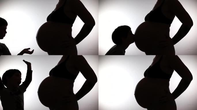 剪影男孩亲吻腹部怀孕的母亲。家庭中的期望生育孩子