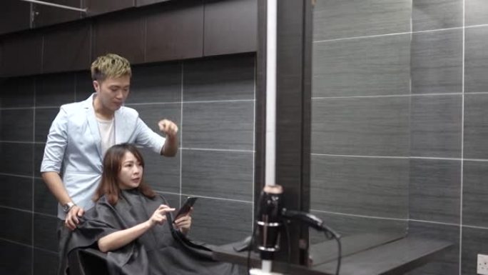 亚洲中国妇女向美发师展示如何使用手机修饰头发