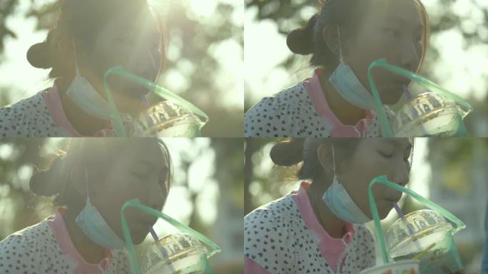 快乐的亚洲女孩在户外公园的塑料玻璃里喝点饮料，带着日落，生活方式的概念。