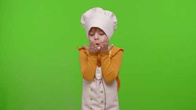 打扮成专业厨师的女童小孩在色度键上将面粉从手中吹入相机