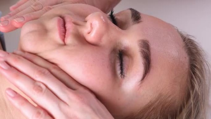 面部按摩美容治疗。特写一名年轻女子的脸躺在背上，得到瘦脸按摩，捏和滚动技术