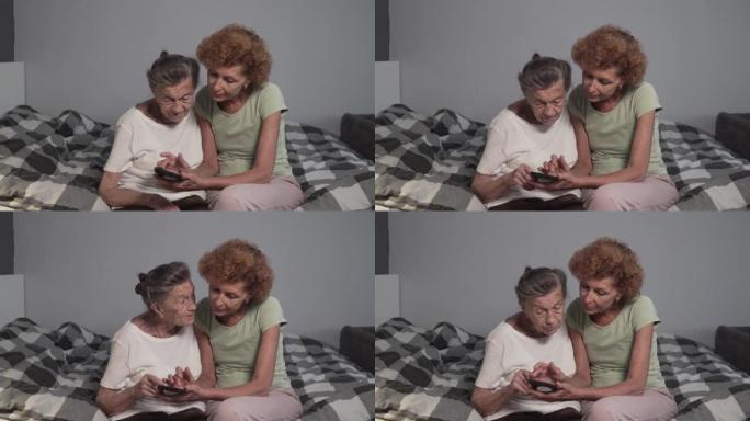 年迈的女儿教她的老母亲使用手机。成熟的护士帮助老年女性如何在疗养院使用智能手机。照顾者和老年人在床上