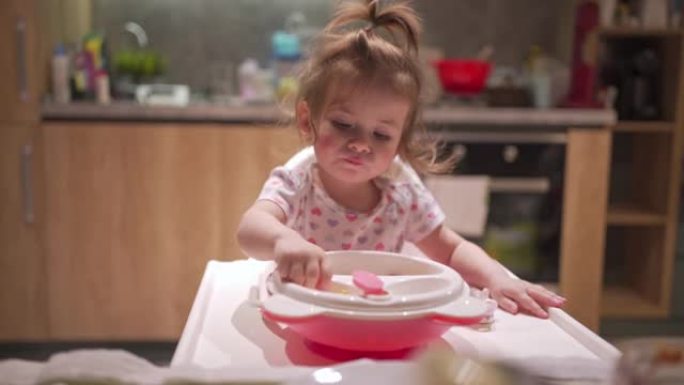 可爱的小女孩，脸蛋红润，在高脚椅上吃饭的时候玩着食碗
