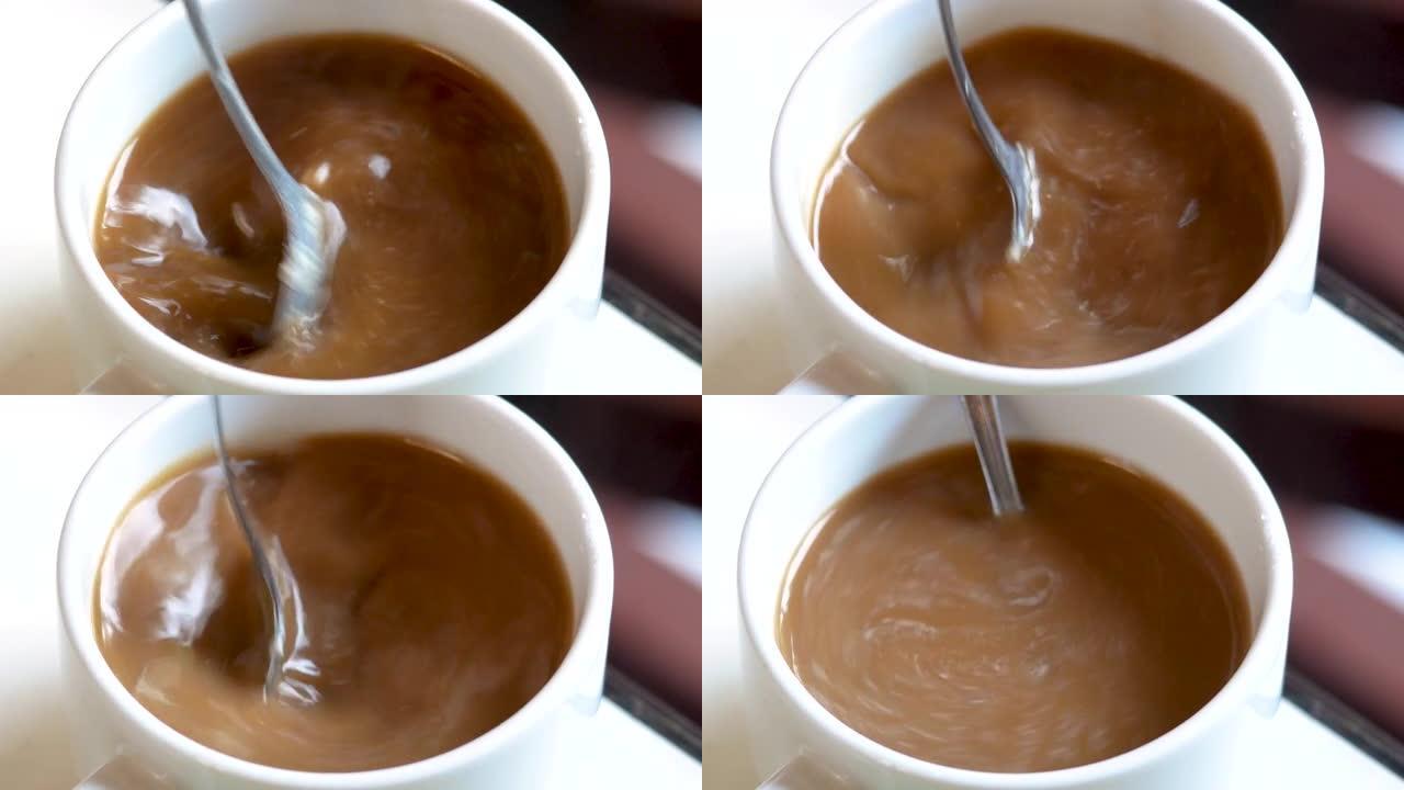 用勺子在一杯芳香咖啡中手工搅拌糖的特写镜头。一杯芳香咖啡放在一张木桌上。