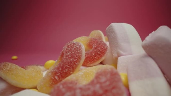 粉红色背景上的棉花糖，果冻豆和彩色酸糖