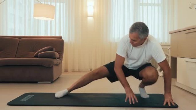 做侧弓步运动的老人。资深男性运动员身体健康热身，在家做腿部伸展运动。照顾好自己的背景现代灯光室。