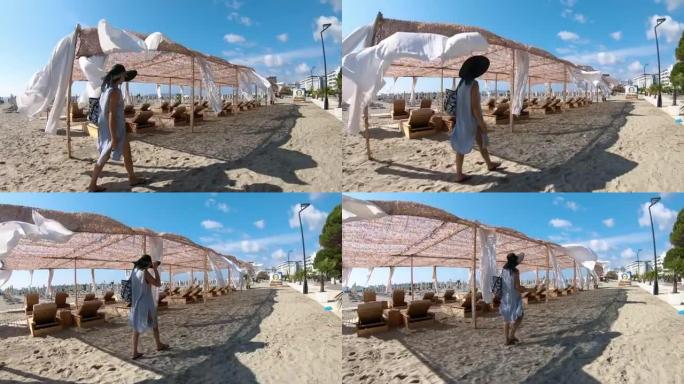 女人走在沙滩上，床铺在沙滩上。海边微风中布艺白色窗帘遮篷