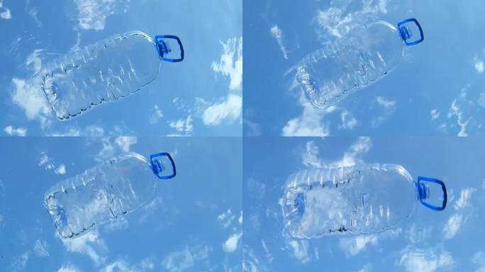 大塑料瓶漂浮在水面上，在蓝天云彩的背景上。带有手柄的桶在海浪上漂移。海洋的塑料污染。水下射击