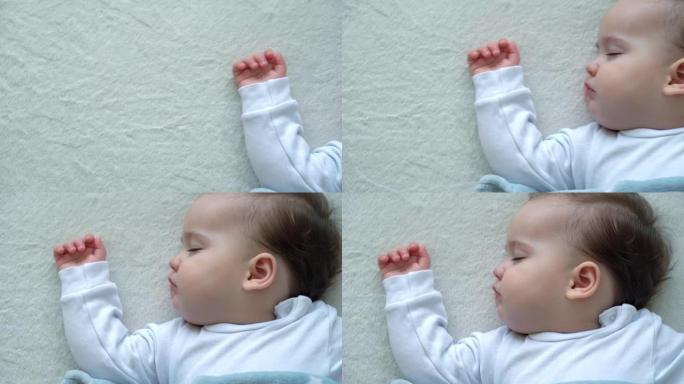 可爱的高加索小婴儿胖乎乎的小女孩的真实特写，睡在舒适的白色床上，铺着蓝色毯子。儿童保育，熟睡的婴儿，