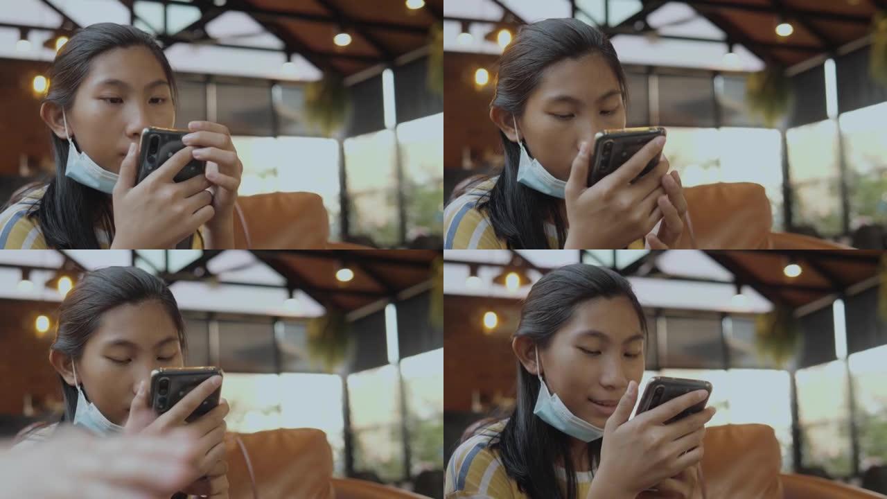 快乐的亚洲女孩戴着口罩，通过智能手机观看病毒视频，坐在沙发上与家人，生活方式的概念。