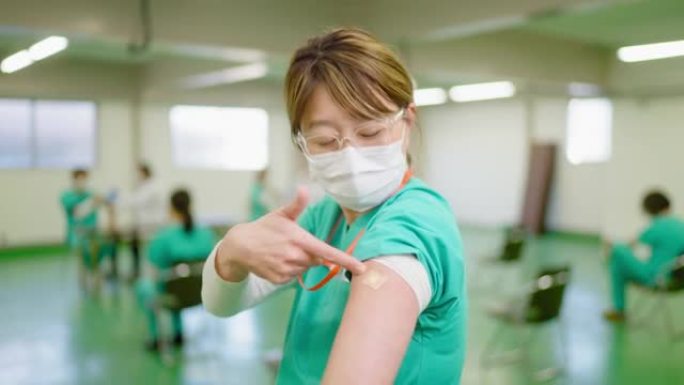 幸福的前线helathcare工作者的肖像在接种疫苗后露出手臂并对着镜头微笑