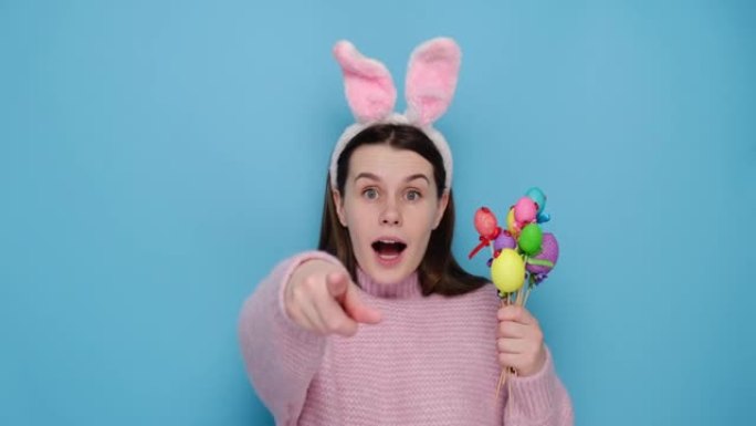 惊呆了的年轻女子对着你对着镜头，春节时是复活节兔子，拿着装饰好的彩蛋，是宗教节日的象征，穿着粉色毛衣