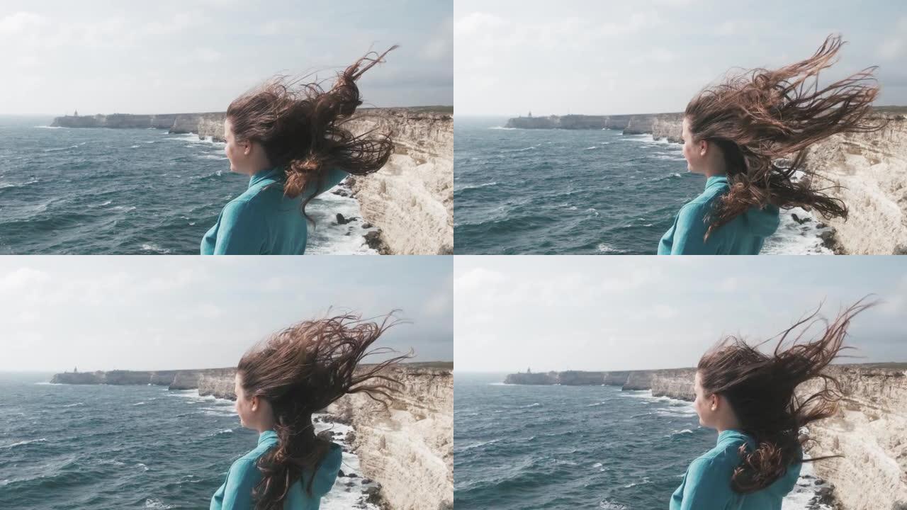 在大风天气里站在海岸线上的年轻女子。
