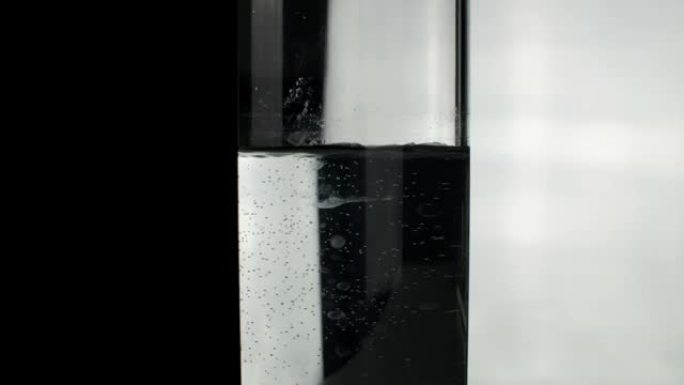 黑白背景上水位降低的玻璃支柱。关闭隔离在黑白背景上的水柱。干净清澈的饮用水。