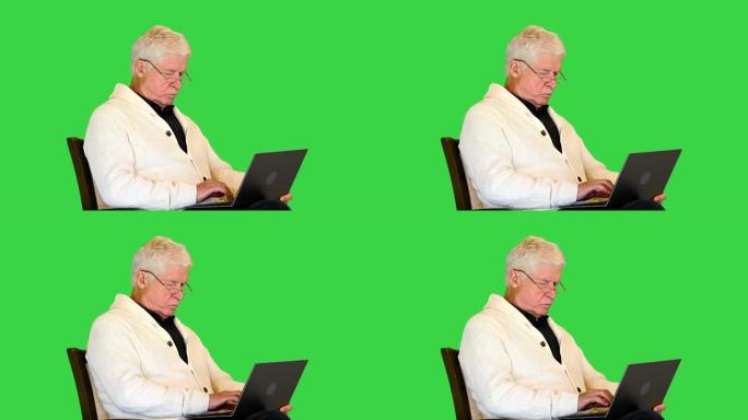 老人坐在扶手椅上，使用绿色屏幕上的笔记本电脑，色度键