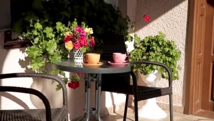 橙色和粉红色的杯子和咖啡或茶站在花间的房子门廊上的桌子上